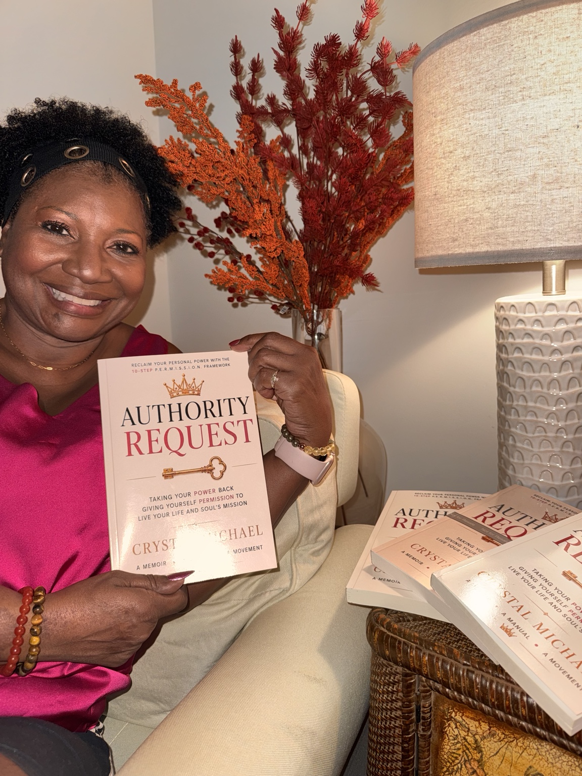 Crystal Michael smiling as she holds up her book Authority Request, with more copies of the book resting beside her.